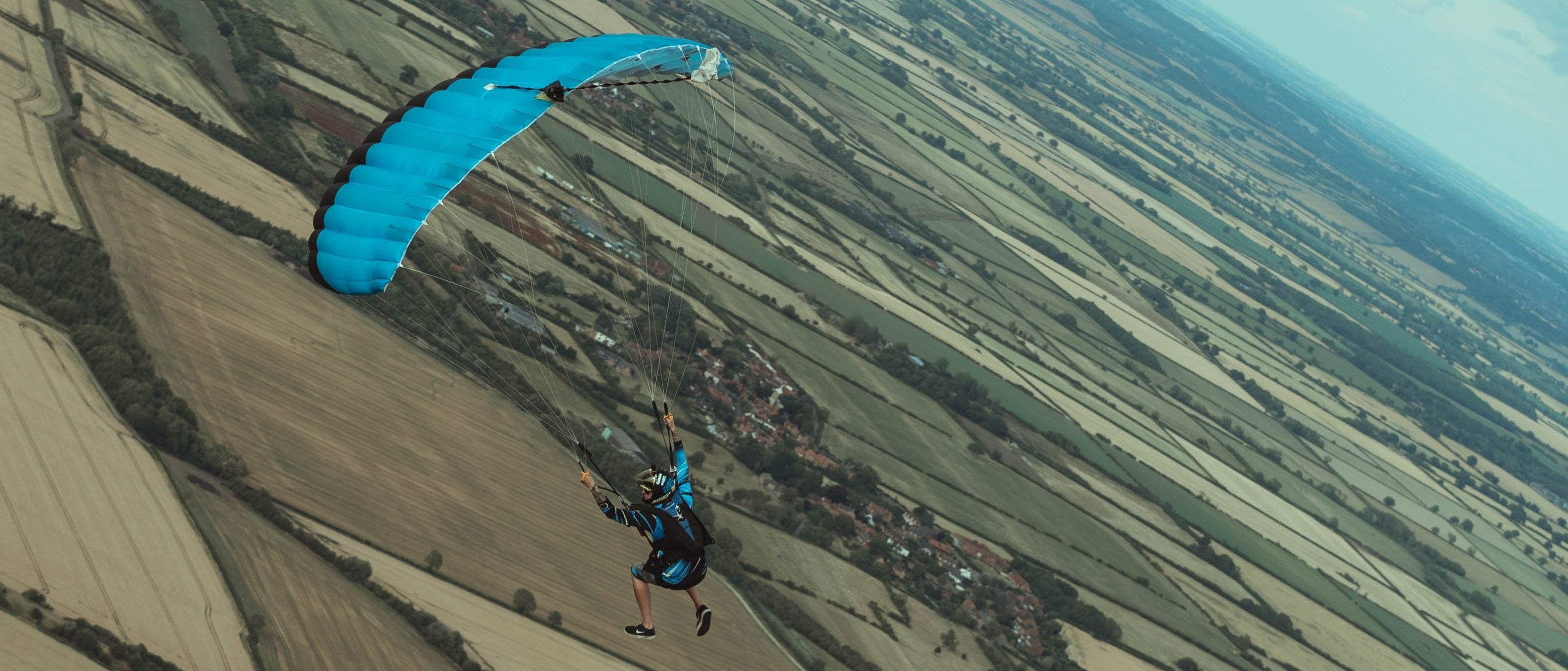 Person skydive over a landscape with a blue parachute